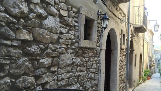 A stone wall with a circular structure, possibly a well or cistern, and a narrow alley with buildings on either side.