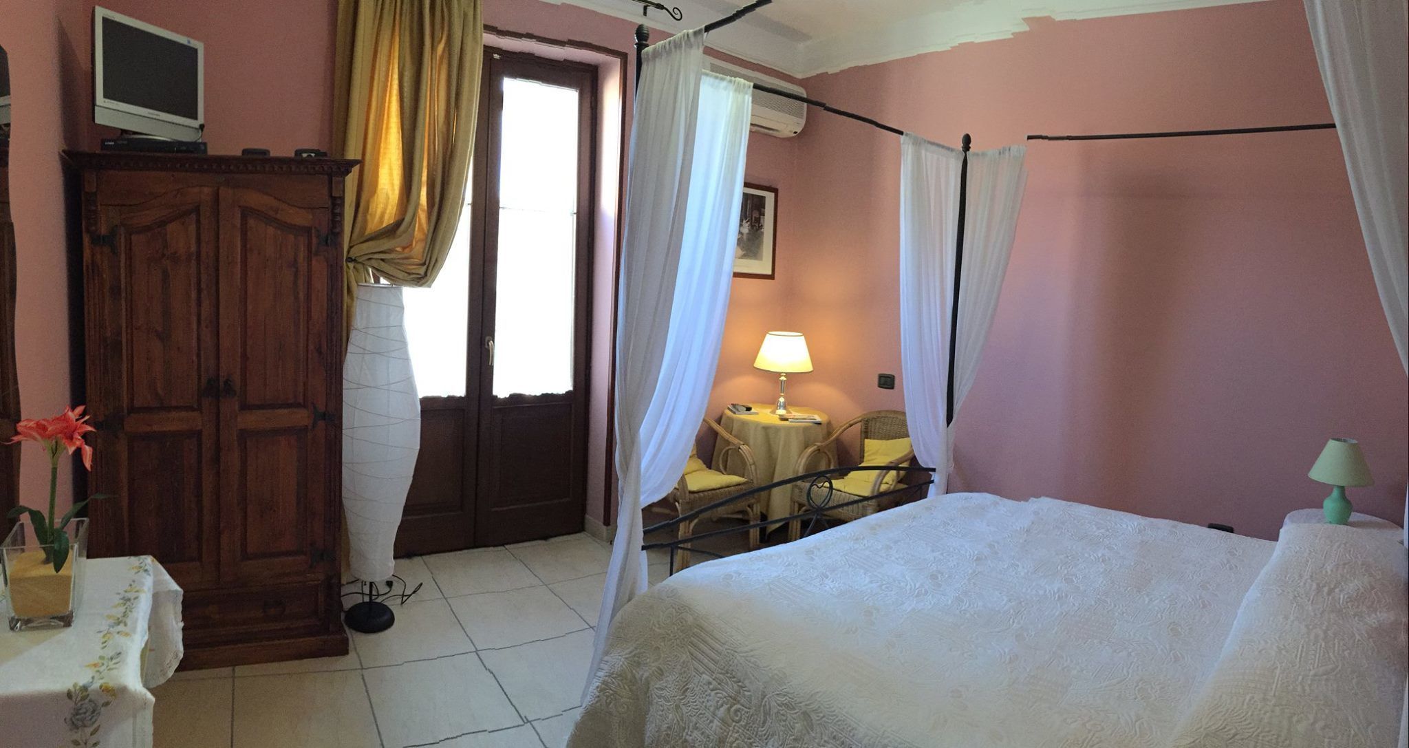 A bedroom with a bed, a wooden wardrobe, a desk with a lamp, and a chair.
