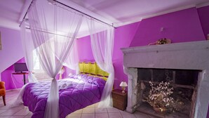 Camera da letto con arredamento viola, un letto a baldacchino, un camino e un tavolino con una lampada.