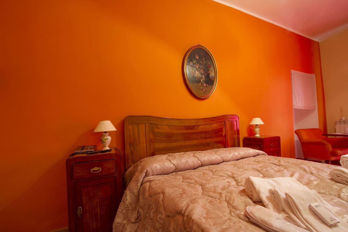 Ein Hotelzimmer mit einem großen Bett, zwei Nachttischen mit Lampen, einem hölzernen Kopfteil, einem Bild an der Wand und einem roten Sessel.