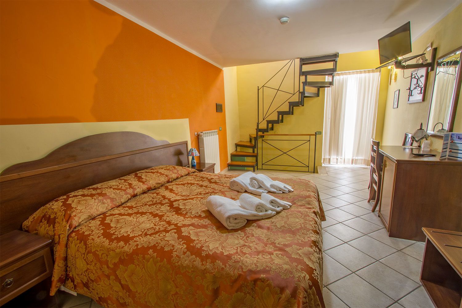 Une chambre d’hôtel avec un grand lit, un bureau, une chaise, un radiateur, un escalier et un téléviseur.