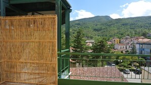 Un balcone con un pannello in bambù, una ringhiera verde e vista su una città con case e una montagna sullo sfondo.