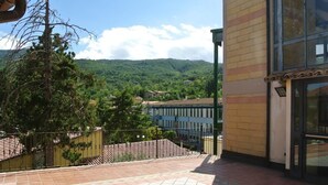 Un edificio con un patio piastrellato, una recinzione in metallo e una vista su un paesaggio verde con alberi e colline sullo sfondo.