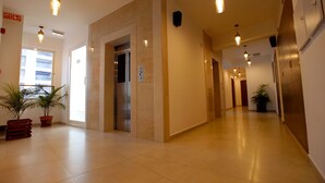 A hotel corridor with a tiled floor, potted plants, a reception desk, and an elevator. - Niko Hotels (Kanayannur)