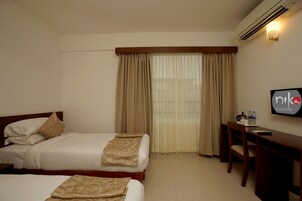 A hotel room with two beds, a desk, and a chair. There is a window with curtains, an air conditioning unit, and a sign on the wall.