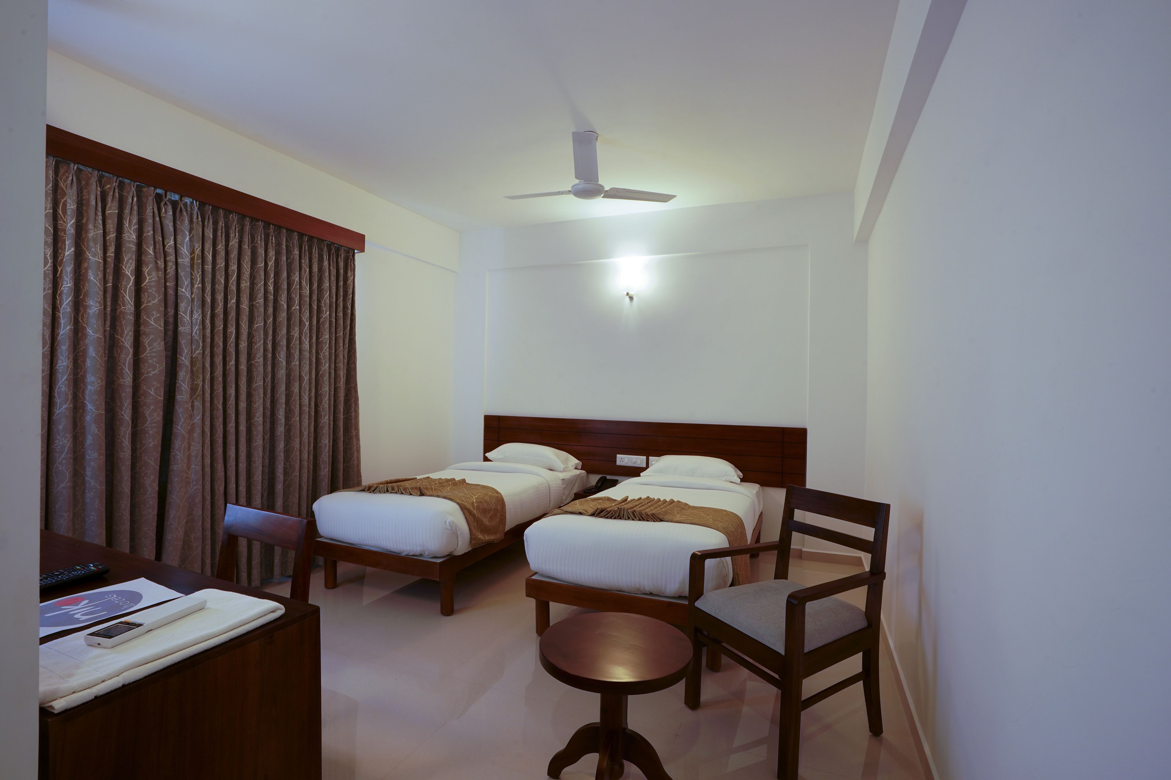 Ein Hotelzimmer mit zwei Betten, einem Schreibtisch mit Stuhl, einem kleinen Tisch und einem Deckenventilator.
