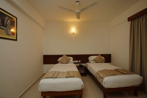 A hotel room with two single beds, a ceiling fan, a nightstand with a phone, and a wall-mounted light.