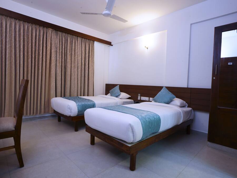 A hotel room with two beds, a ceiling fan, a wooden chair, and a large window with curtains.