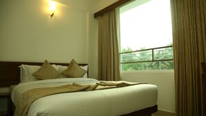 A neatly made bed with a wooden headboard and two pillows, a window with curtains, and a wall-mounted light fixture. - Niko Hotels (Kanayannur)