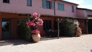 A pink building with a gravel courtyard, outdoor seating, and large potted plants. - Agriturismo Fattoria Il Casalone (Orbetello)