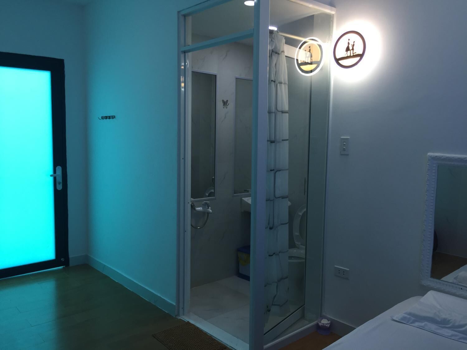 Et hotelværelse med en glasafskærmet bruseniche, en seng med hvide sengetøj og en dør med en neonreklame.