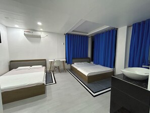 Habitación de hotel con dos camas, un escritorio, una silla, baño con lavamanos y ventana con cortinas.