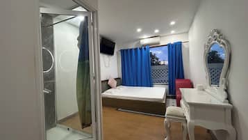 Una habitación con cama, escritorio, silla, televisión y ventana con cortinas.