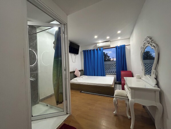 Una habitación con cama, escritorio, silla, televisión y ventana con cortinas.