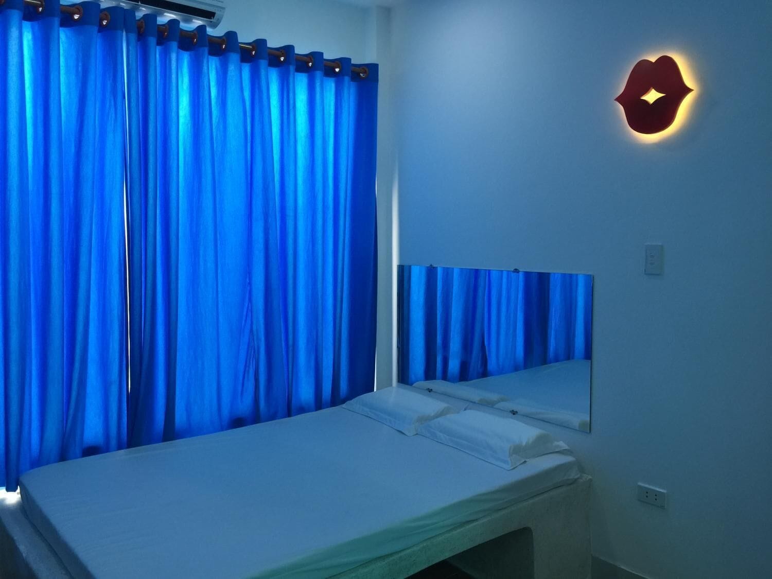 Una habitación con cama, cortinas azules y una lámpara fijada a la pared.