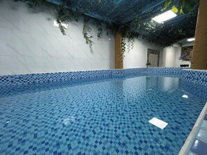 Una piscina amb mosaics blaus, envoltada per parets amb un disseny blanc i blau i un sostre amb vegetació artificial.