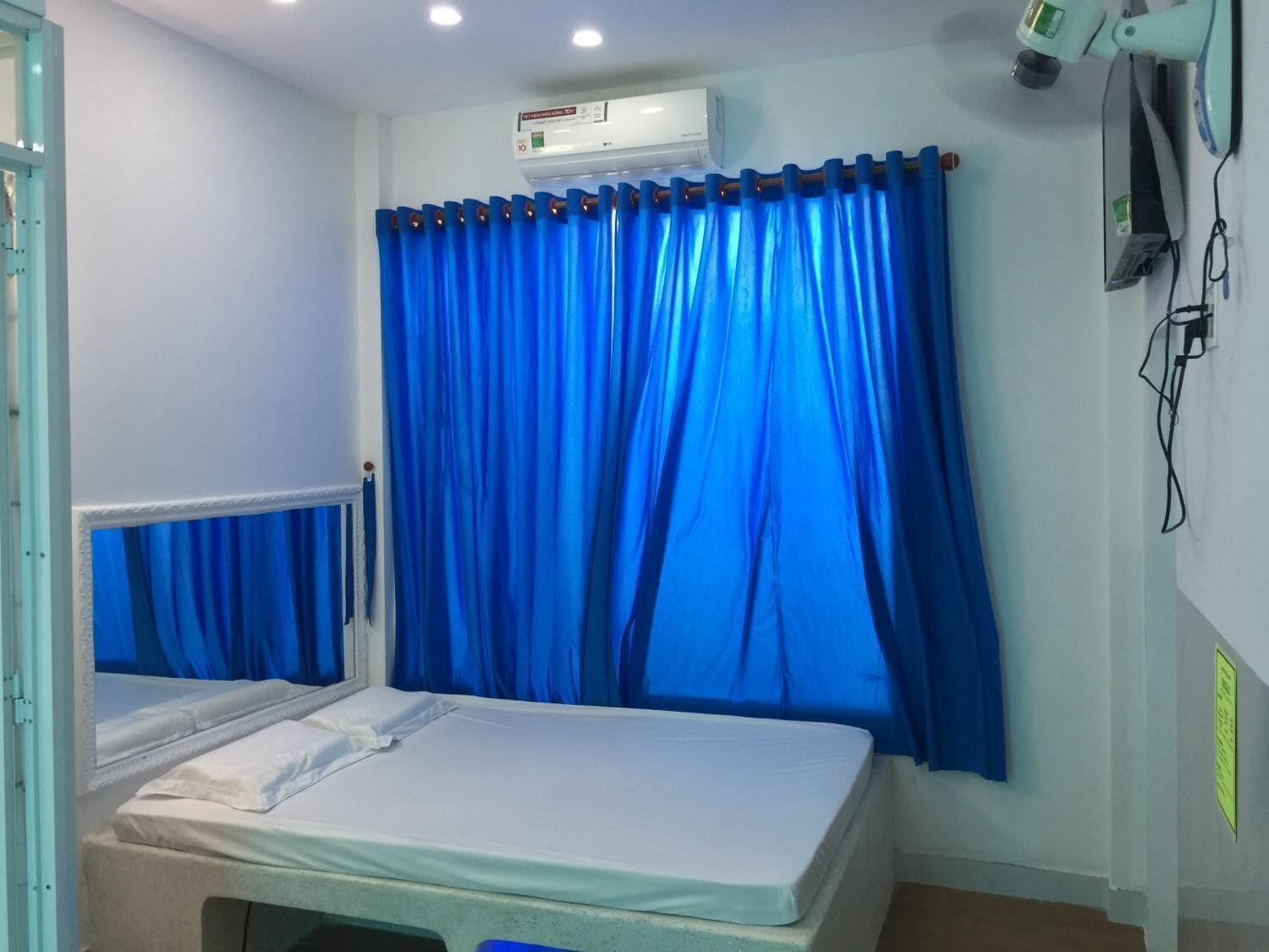 Ein Krankenzimmer mit einem Bett, einem Fenster mit blauen Vorhängen, einer Klimaanlage und medizinischer Ausrüstung an der Wand.