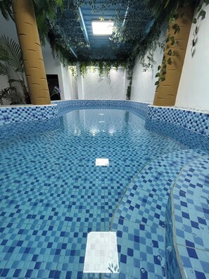 Una piscina interior con mosaicos azules, rodeada de paredes con vegetación vertical y un techo con plantas colgantes.