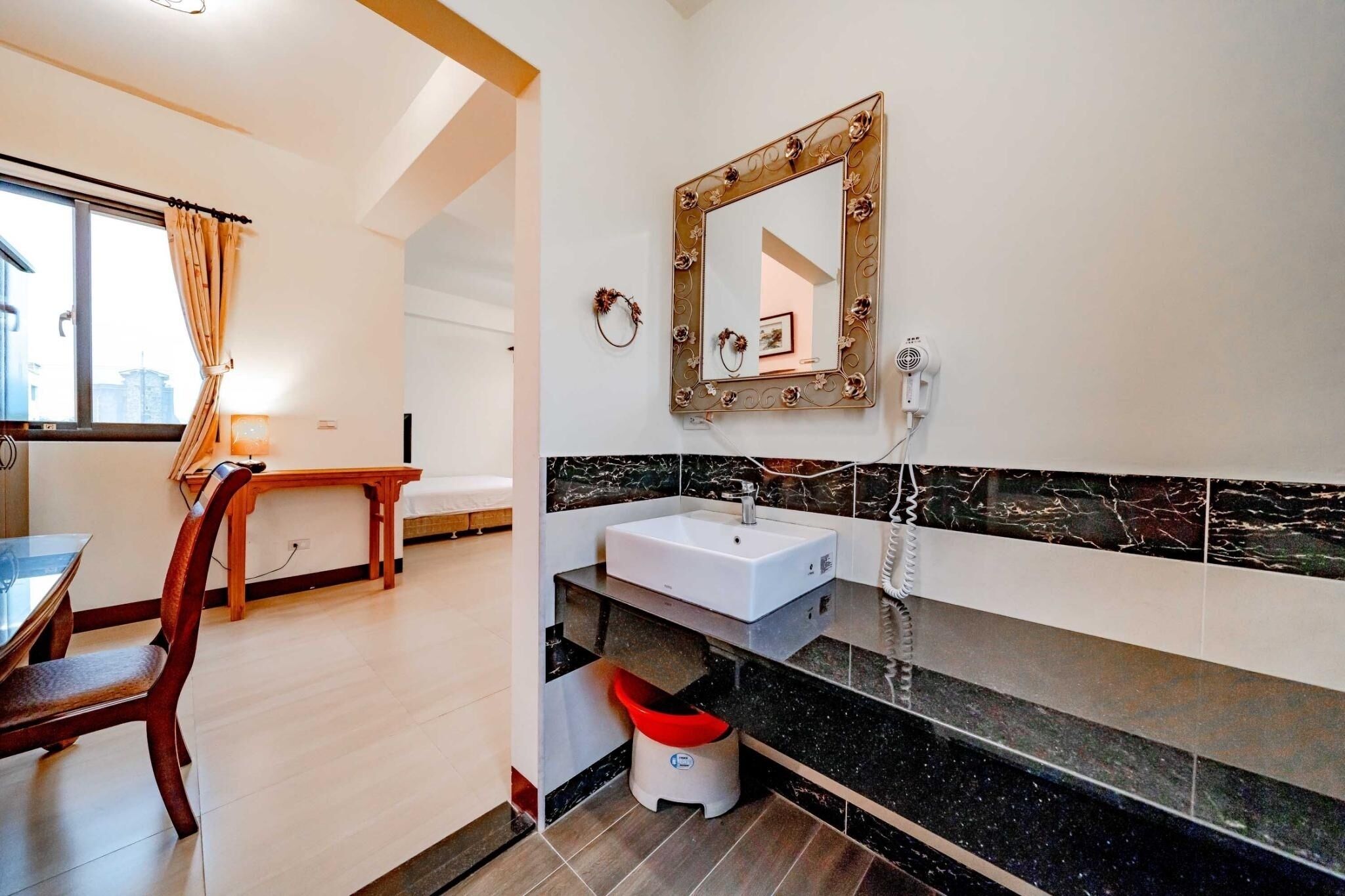 A modern bathroom with a marble sink, a decorative mirror, and a small trash bin.