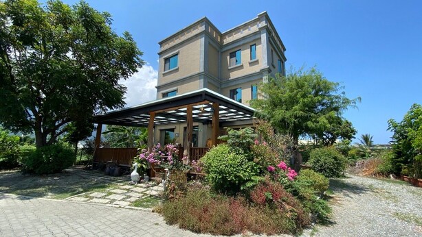 A two-story building with a covered patio area, surrounded by lush greenery and flowering plants. - Bo Jue Farm Stay (Ji'an)