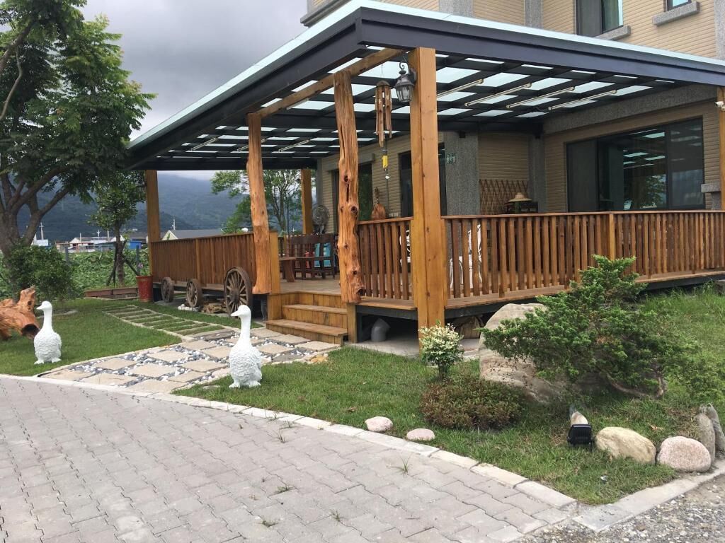 A wooden deck with a pergola, a stone pathway, and a small garden with rocks and a bird sculpture.