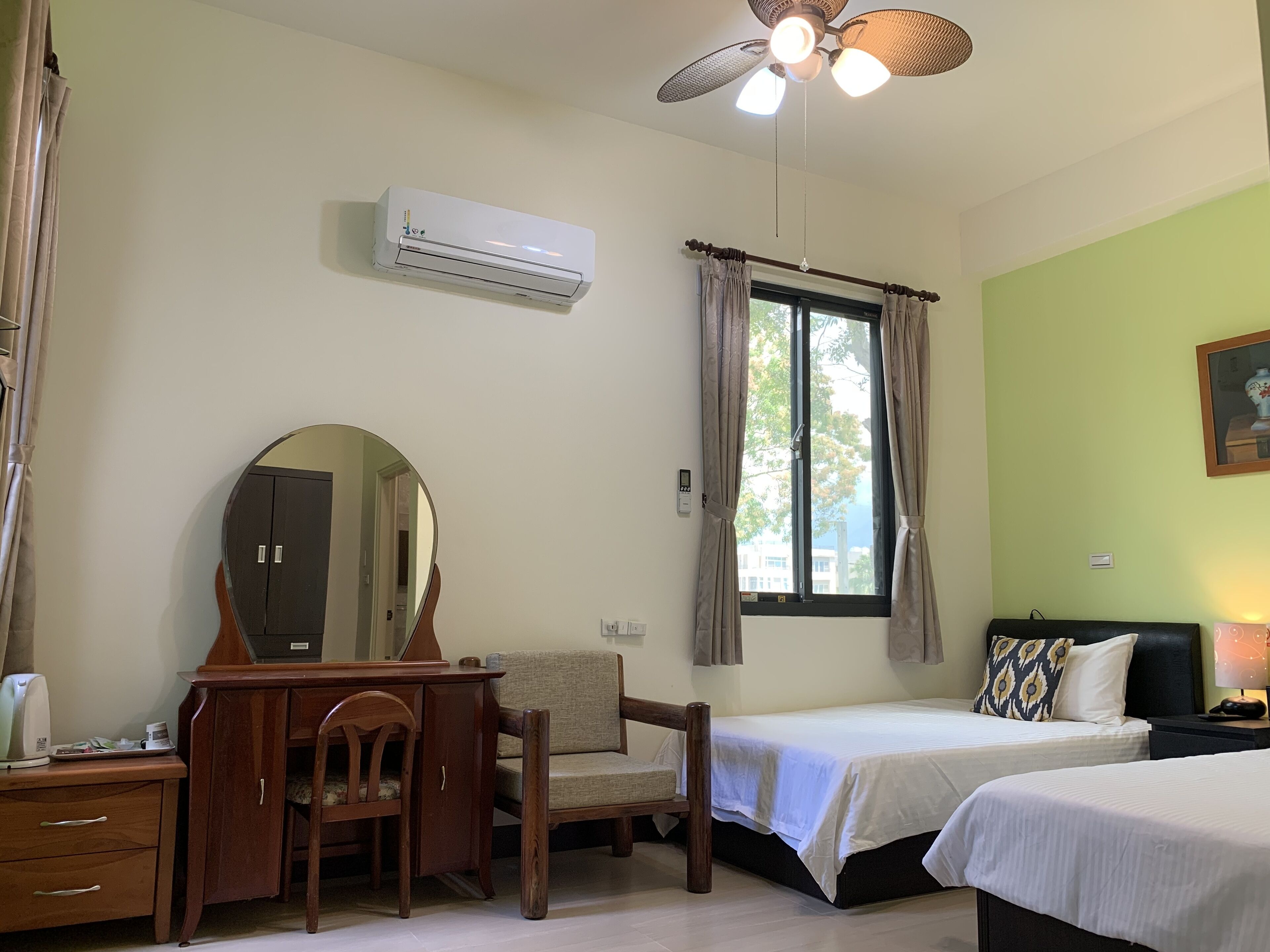 Una habitación con cama, escritorio, silla, aire acondicionado, ventilador de techo y ventana con cortinas.