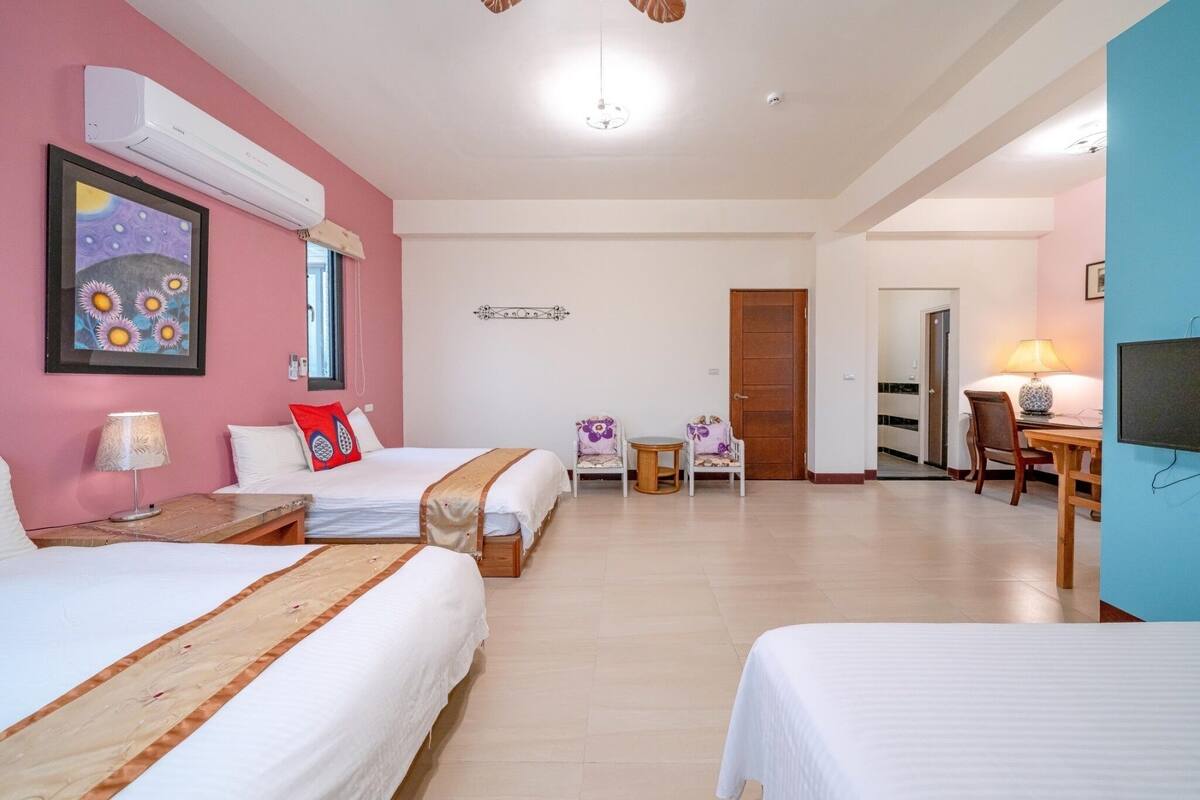 A hotel room with two beds, a desk, a chair, a small table, and a TV.