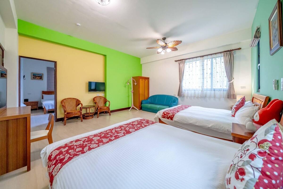A hotel room with two beds, a desk, a television, and a window with curtains.