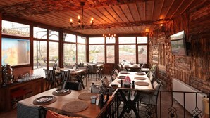 A rustic dining area with wooden tables and chairs, large windows, and a chandelier.