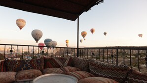 A balcony with a sofa and a table, overlooking a desert landscape with hot air balloons in the distance. - Rose Valley Hotel (Avanos)