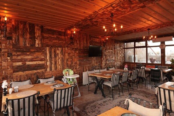 A rustic dining area with wooden walls, a television mounted on the wall, and a variety of seating arrangements including tables and chairs.