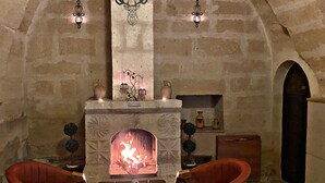 A stone-walled room with a fireplace, two red chairs, a wooden table, and decorative wall sconces.