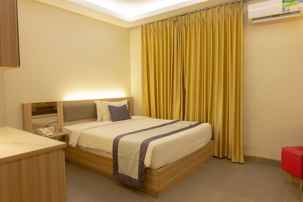 A hotel room with a bed, bedside table, and a red chair.