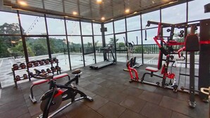 Un gimnasio con diferentes equipos de ejercicio, ventanas amplias y vistas al exterior.