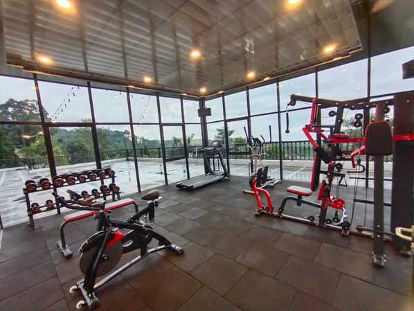 Un gimnasio con diferentes equipos de ejercicio, ventanas amplias y vistas al exterior.