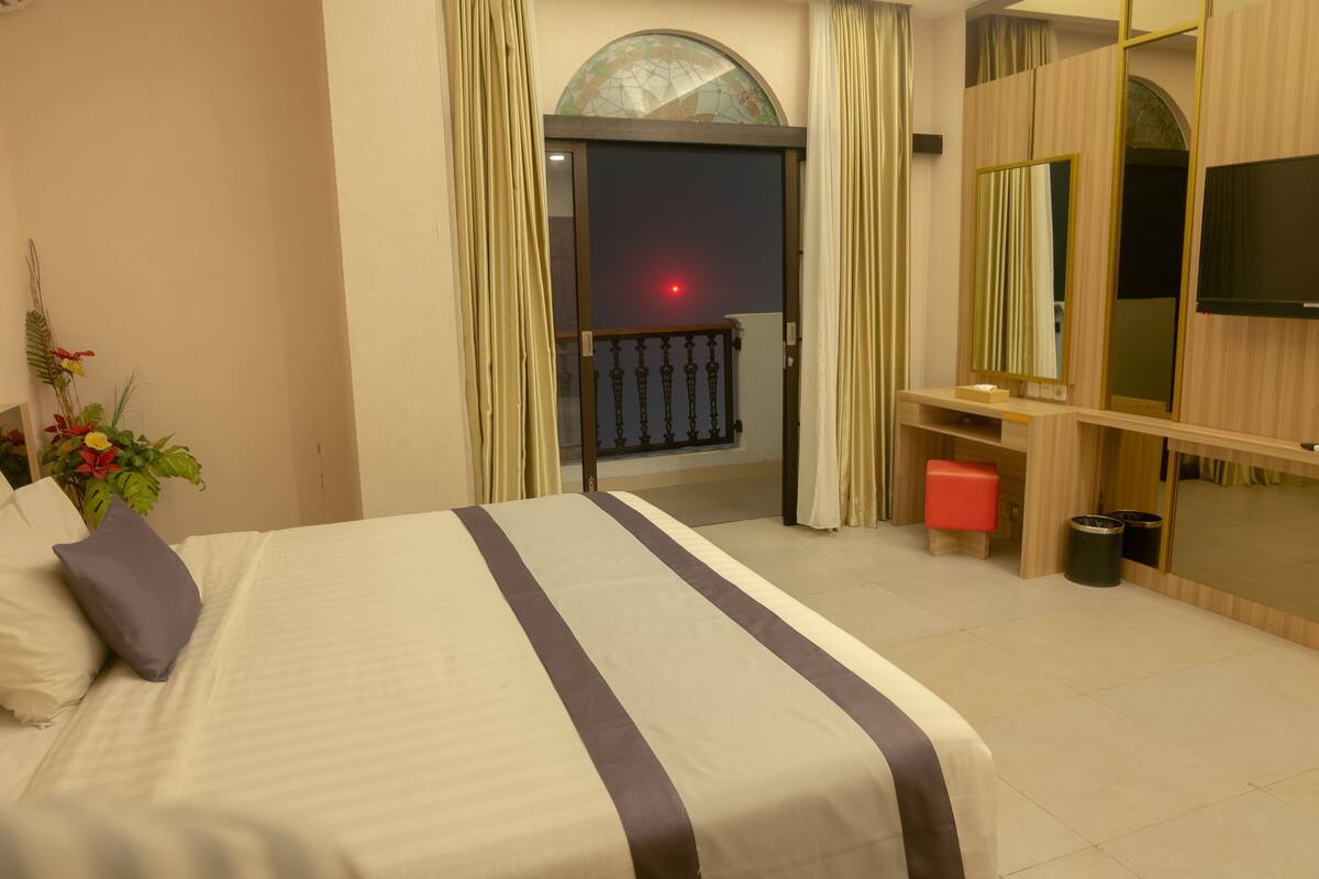 A hotel room with a bed, a TV, a mirror, a small table, and a balcony with a view.