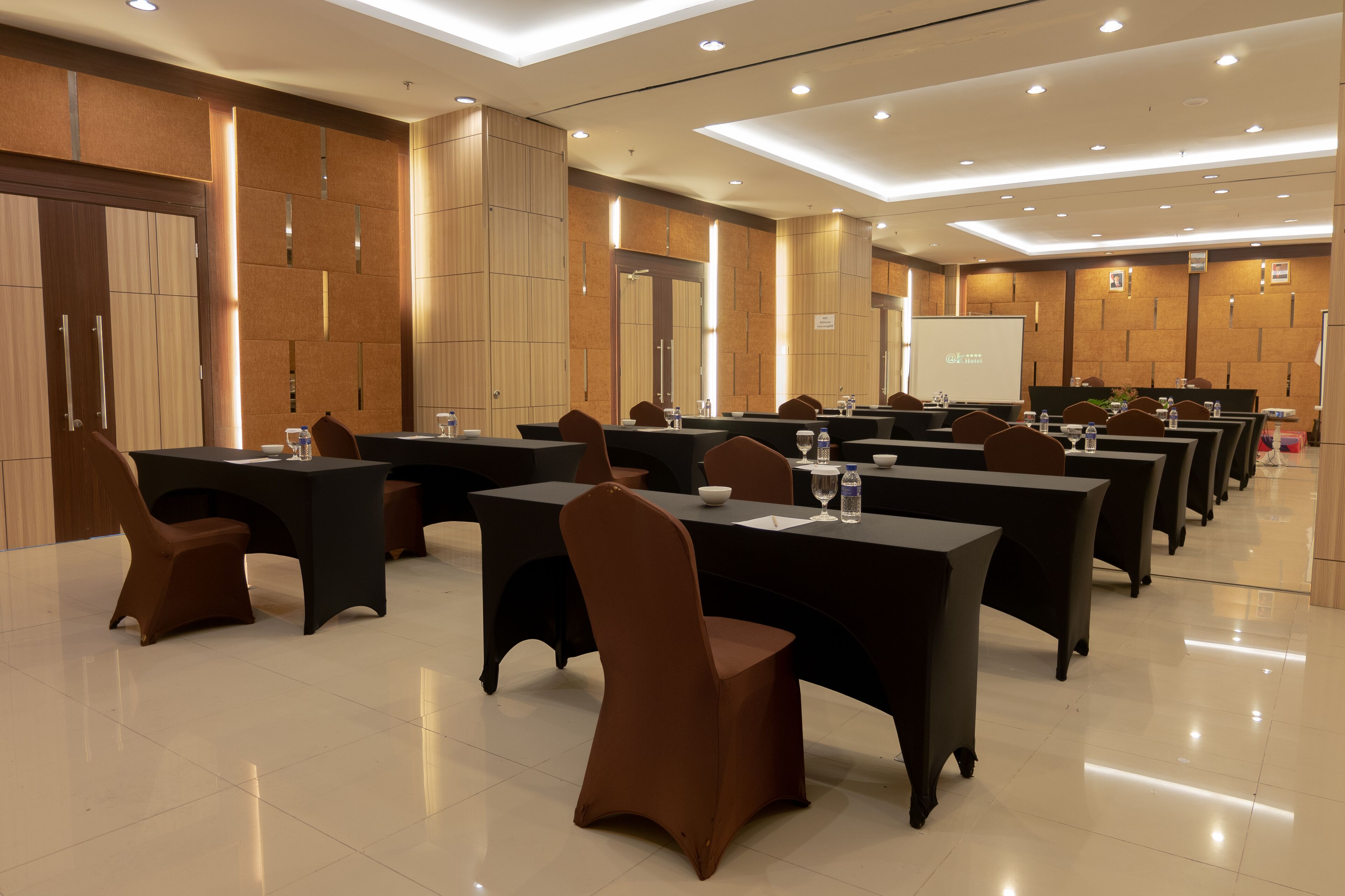 A conference room with multiple tables and chairs, equipped with water bottles and a projector screen.