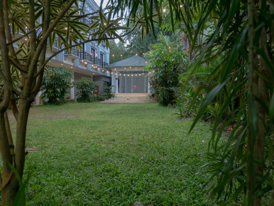 A courtyard with a building in the background, surrounded by greenery and string lights.