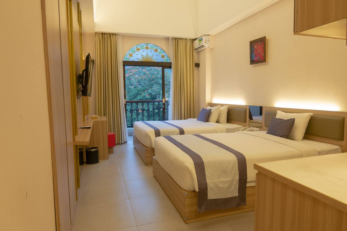 A hotel room with two beds, a balcony, a TV, and a painting on the wall.