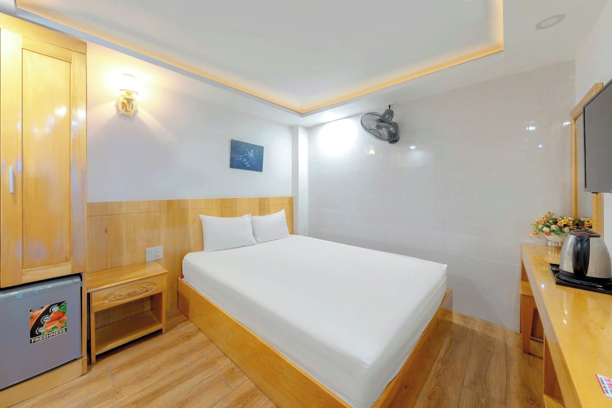 Une chambre d’hôtel équipée d’un lit, d’un petit bureau avec une bouilloire, d’un réfrigérateur et d’un ventilateur fixé au mur.