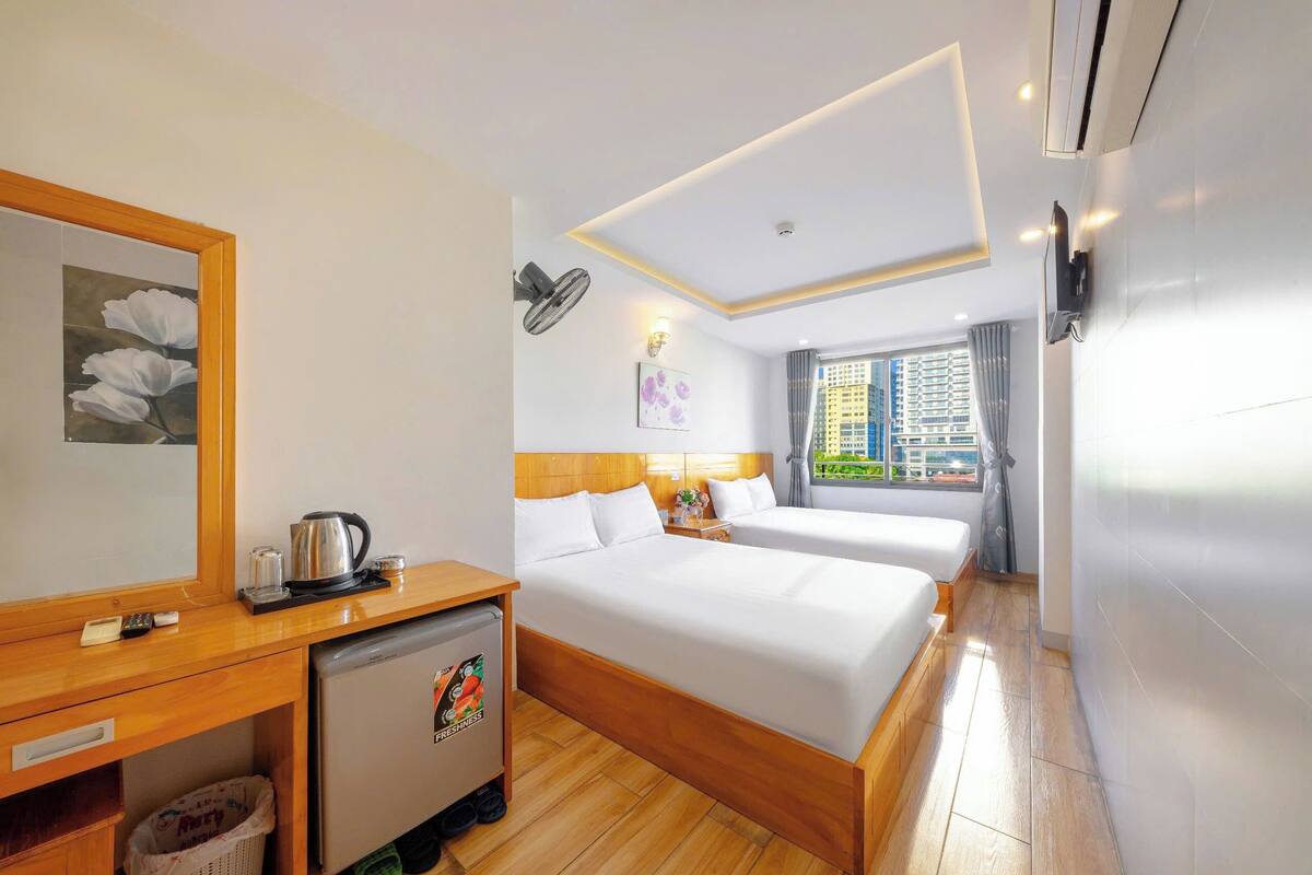 Une chambre d’hôtel avec deux lits, un petit bureau avec une bouilloire, un réfrigérateur et une fenêtre donnant sur la ville.