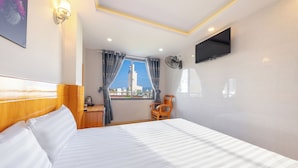 Une chambre d’hôtel avec un lit, un téléviseur fixé au mur, une fenêtre avec des rideaux et une vue sur un bâtiment à l’extérieur.