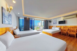 Ein Hotelzimmer mit zwei Betten, einem Balkon mit Blick auf Gebäude, einem Wand-Fernseher und einem Deckenventilator.