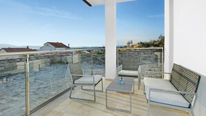 Une terrasse sur le toit, dotée d’une balustrade en verre, de deux fauteuils confortables, d’une petite table et offrant une vue sur la mer et les bâtiments éloignés.
