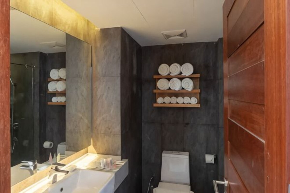 A bathroom with a large mirror, a sink, a toilet, and shelves with towels.