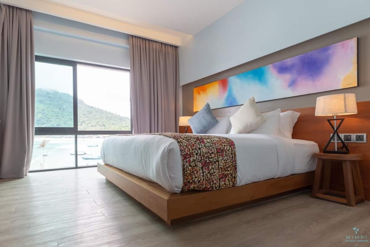A hotel room with a large bed, a view of the sea, and a colorful abstract painting on the wall.