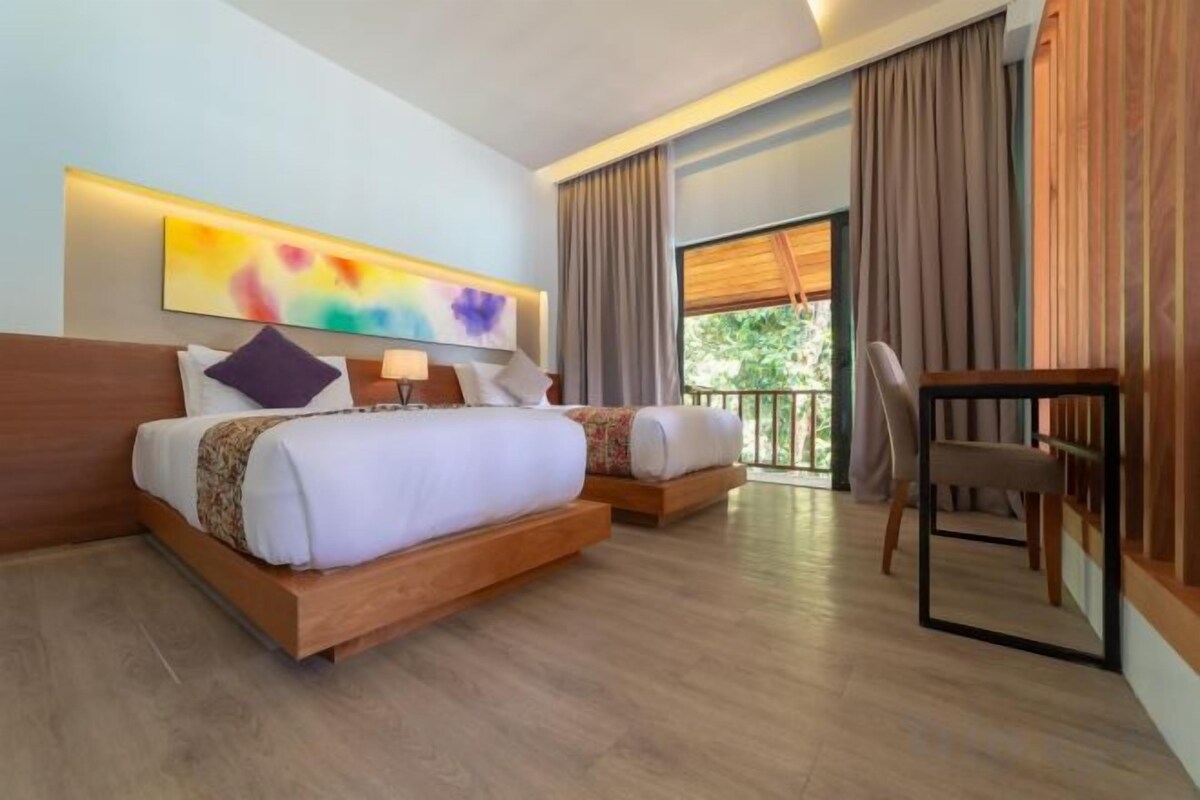 Habitación de hotel con una cama grande, una mesita de noche, una silla y un ventanal con cortinas.