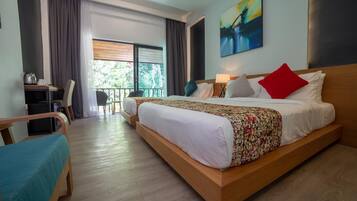 A hotel room with a large bed, a desk, and a chair. There is a balcony with a view of greenery.