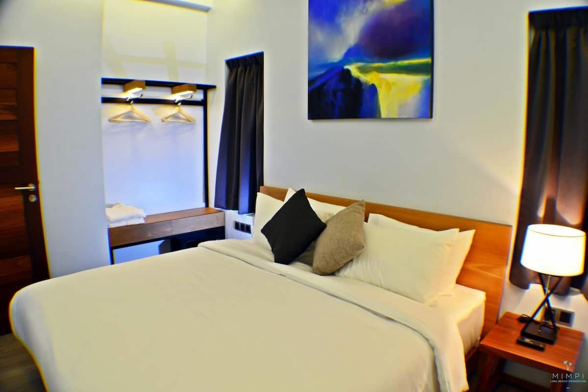 A hotel room with a large bed, a bedside table with a lamp, a wall-mounted TV, and a painting above the bed.