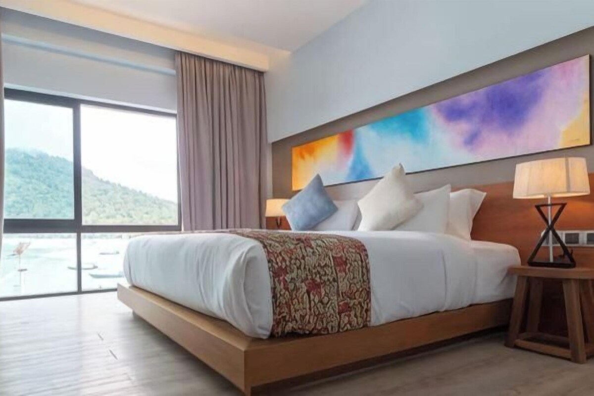 A hotel room with a large bed, a view of the outdoors, and a painting on the wall.